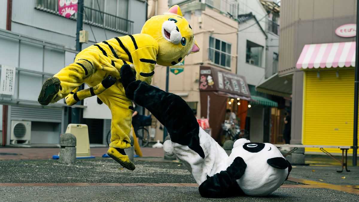 Un combat entre deux personnages vêtus de costumes d'animaux de grande taille, alors qu'un panda assis par terre donne un coup de pied dans le ventre d'un tigre qui bondit, dans Baby Assassins 2.