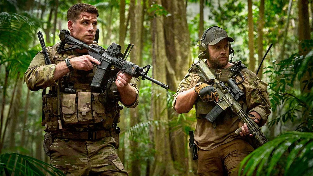 Deux hommes en tenue de camouflage militaire tenant des fusils dans une forêt tropicale.