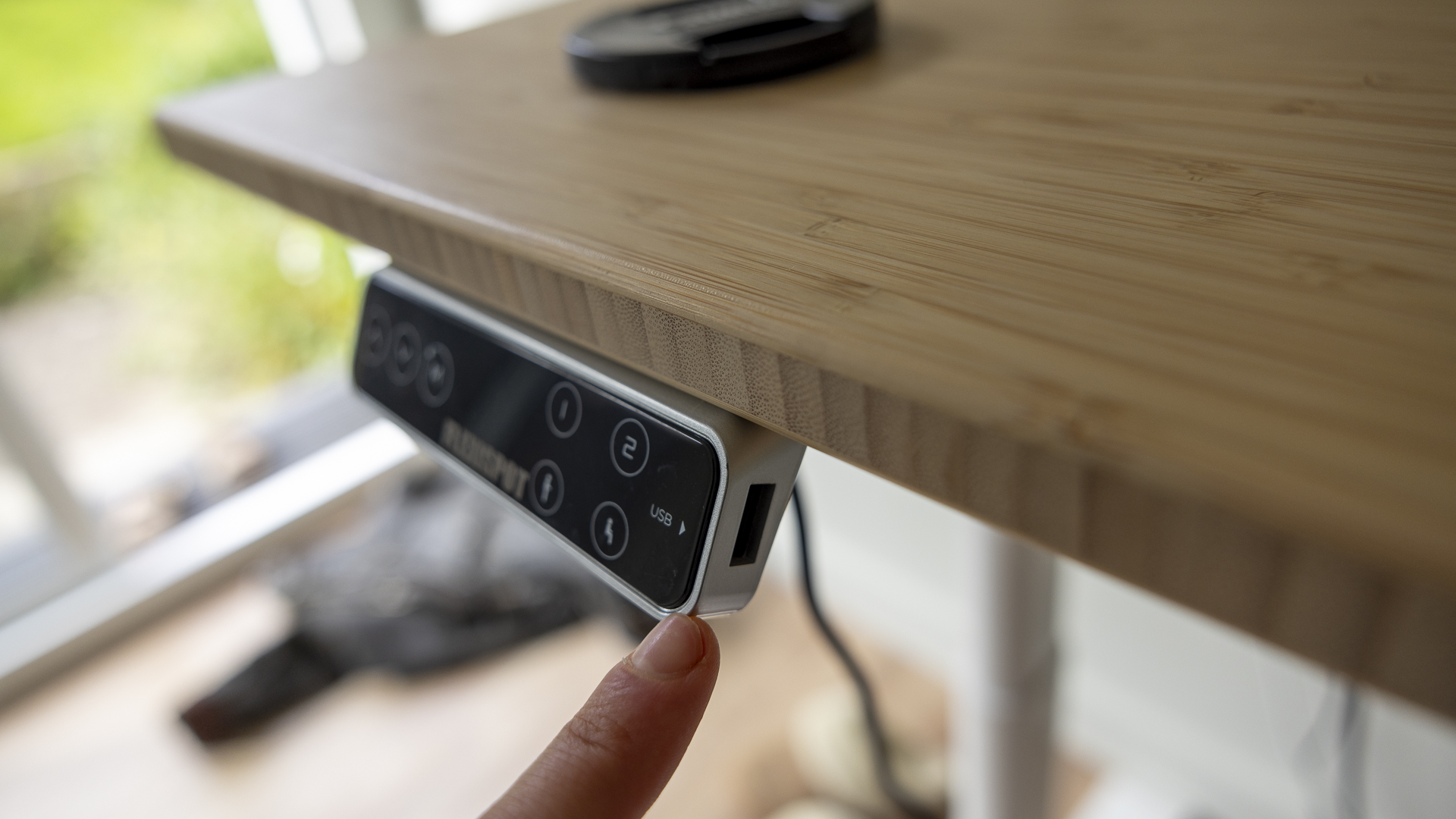 Image d'examen du bureau debout Flexispot E8 montrant le panneau USB avec un petit doigt venant vers lui.