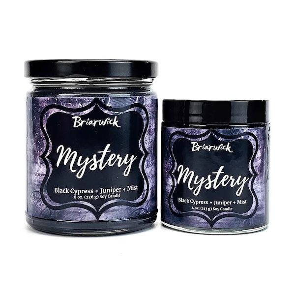 Deux bougies d'une société appelée Briarwick, l'une plus grande que l'autre, contiennent toutes deux des étiquettes violettes et noires ainsi que le nom "Mystère"