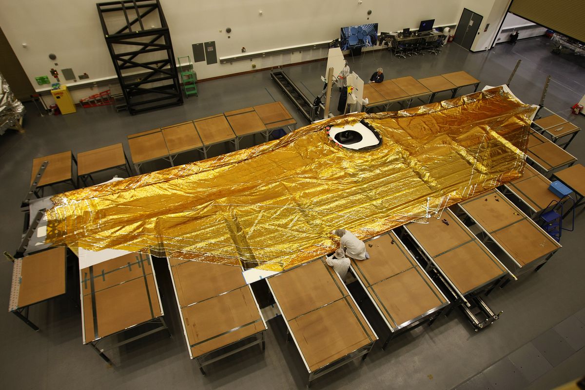 Un pare-soleil doré à cinq couches étendu sur un morceau du télescope spatial James Webb posé sur le sol