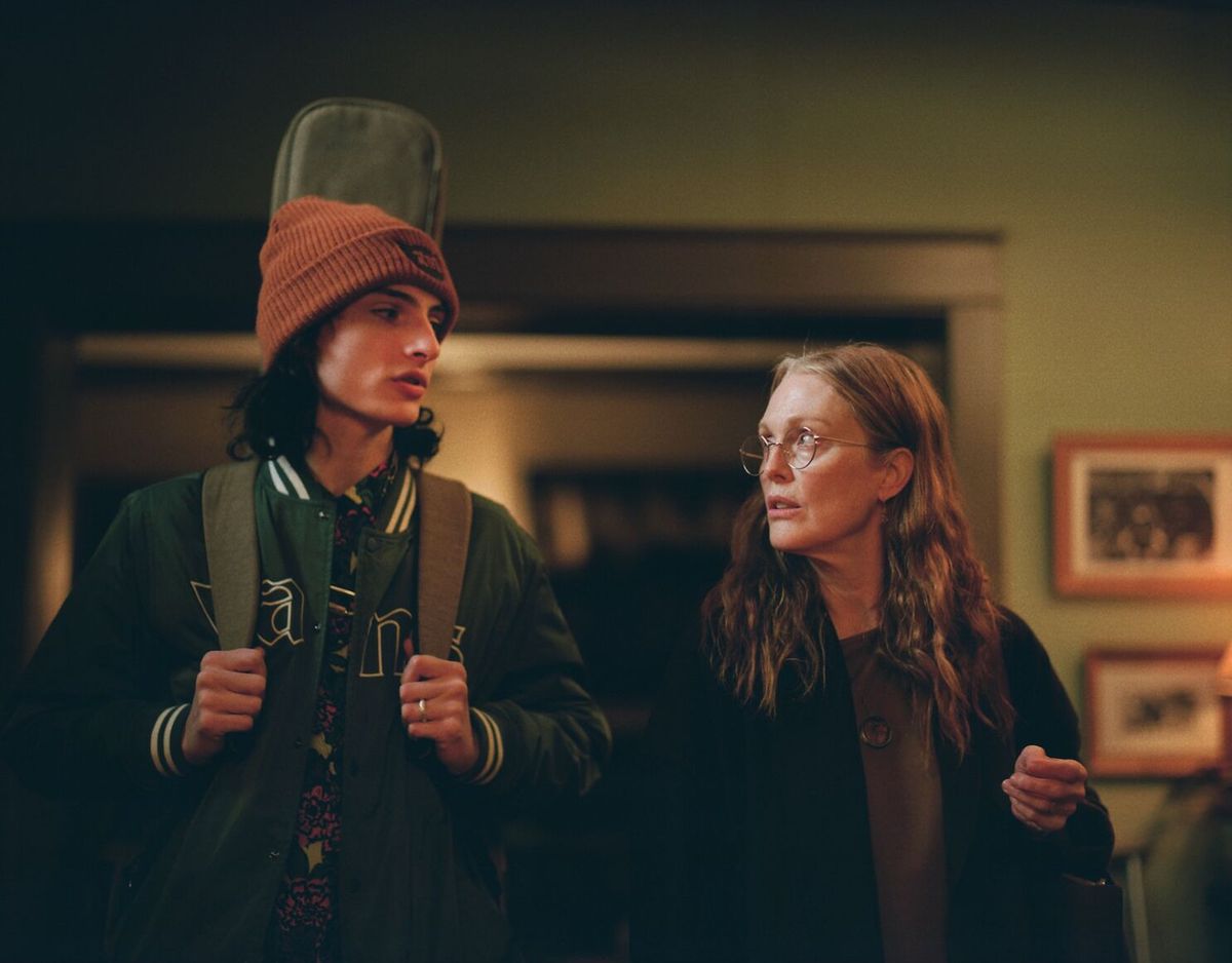Un adolescent (Finn Wolfhard) avec un étui de guitare sur le dos se tient à côté d'une femme plus âgée aux cheveux longs (Julianne Moore) qui porte des lunettes.