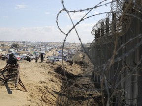 Des Palestiniens déplacés par l'offensive aérienne et terrestre israélienne dans la bande de Gaza sont assis à côté de la barrière frontalière avec l'Égypte à Rafah, le mercredi 24 janvier 2024.