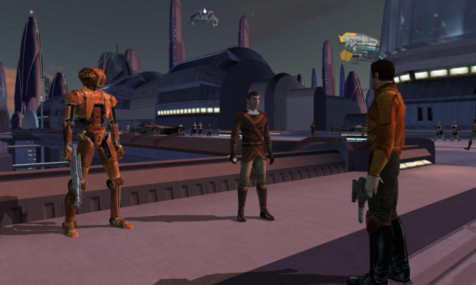 Extrait de Star Wars : Les Chevaliers de l'Ancienne République.  Deux personnes et un droïde se tiennent dehors sur un pont dans un environnement très Star Wars.  Bâtiments, navires, tours.